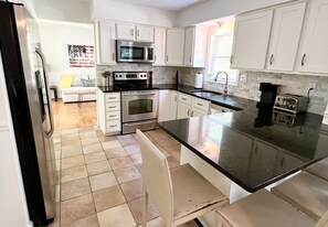 Cozinha moderna com armários brancos, bancada preta, geladeira de aço inoxidável, micro-ondas, forno e cafeteira.