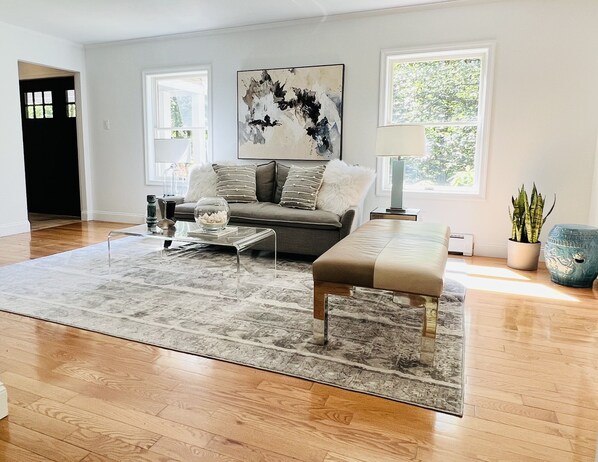 Uma sala de estar moderna com um sofá cinzento, uma mesa de centro de vidro, um banco e um grande quadro abstrato.
