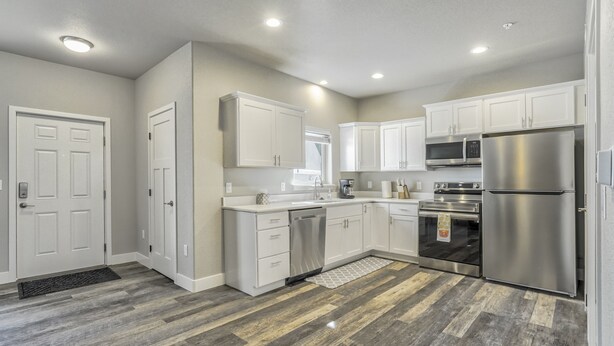 A modern kitchen with white cabinets, stainless steel appliances, and a herringbone wood floor.