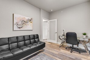 A modern living room with a black leather sofa, a glass coffee table, and a minimalist desk with a chair.