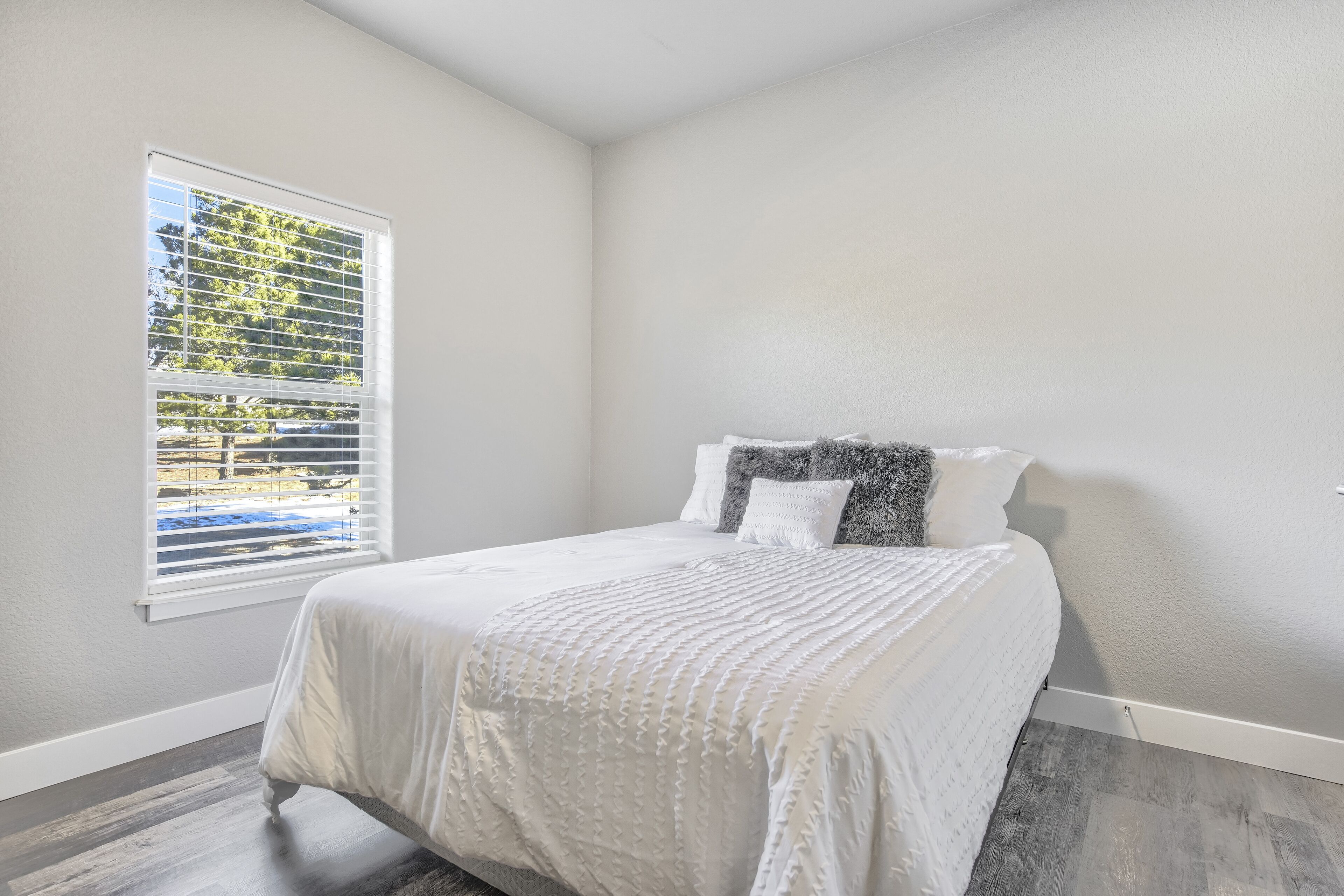 Une chambre à coucher avec un lit, une fenêtre avec des stores et une vue sur les arbres à l’extérieur.