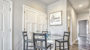 Un área de comedor con una mesa redonda de cristal y cuatro sillas, una puerta blanca y un letrero en la pared que dice 