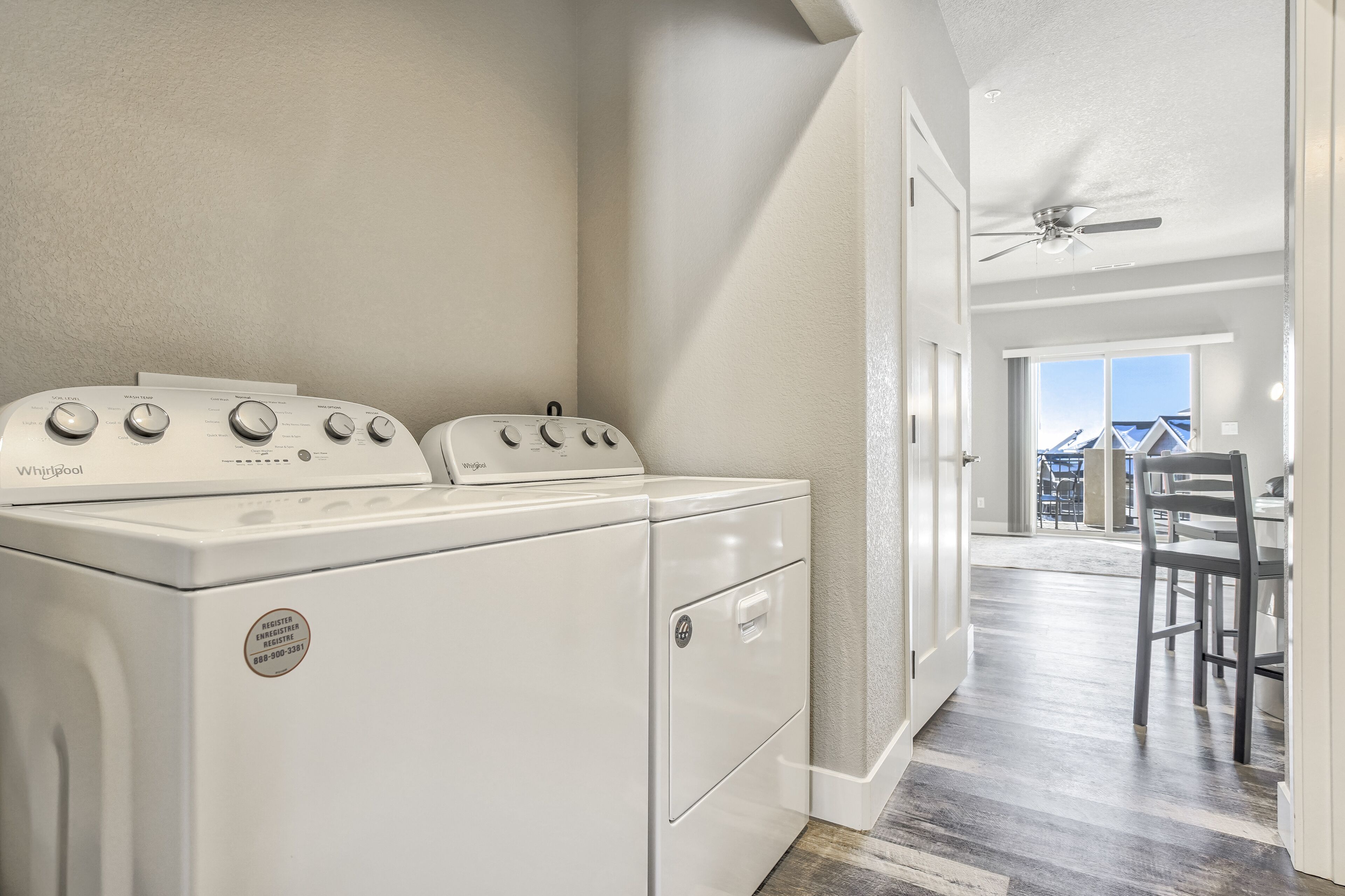 Una lavanderia con lavatrice e asciugatrice Whirlpool, una ventola a soffitto e vista su un'area pranzo con tavolo e sedie.