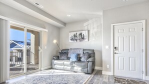Una sala de estar moderna con un sofá de cuero gris, un tapete estampado y un cuadro con una vista urbana en la pared.