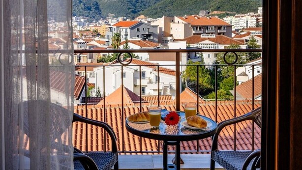 A balcony with a table set for breakfast, overlooking a cityscape with terracotta-roofed buildings and a hill in the background. - Arvala Apartments  - Apartment with Balcony (Budva)