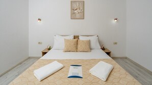 A hotel room with a bed, two bedside tables, a nightstand, a framed artwork on the wall, and a towel and brochure on the bed. - Arvala Apartments  - Apartment with Balcony (Budva)