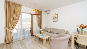 A living room with a sofa, a coffee table, a dining table with chairs, and a window with curtains. - Arvala Apartments  - Apartment with Balcony (Budva)