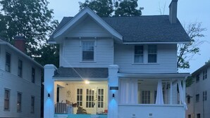 A two-story house with a front porch, a staircase, and a wooden fence. - Historic 1910 Estate · Sleeps 24 · Five Points South · Tea Olive & Azalea (Birmingham)