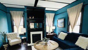 A living room with a blue sofa, a white armchair, a wooden coffee table, and a fireplace. - Historic 1910 Estate · Sleeps 24 · Five Points South · Tea Olive & Azalea (Birmingham)