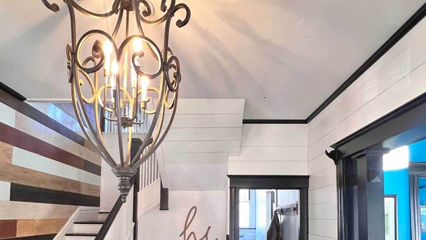 A staircase with black and white railings, a chandelier, and a hallway leading to another room. - Historic 1910 Estate · Sleeps 24 · Five Points South · Tea Olive & Azalea (Birmingham)