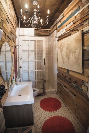 Une salle de bain rustique avec un intérieur en bois, un lavabo blanc, des toilettes, une douche et un lustre.