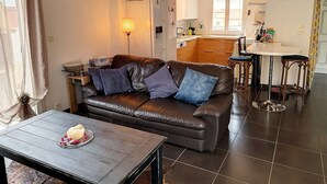 Un salon moderne avec un canapé en cuir, une table à manger illuminée par une bougie, et une cuisine en arrière-plan.