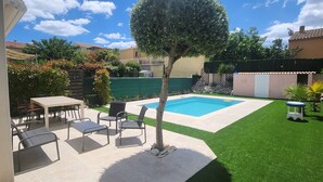 Un jardin avec une piscine, une terrasse avec des chaises et une pelouse bien entretenue.