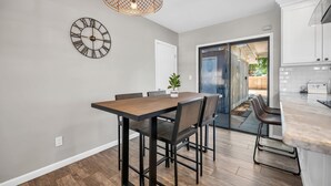A modern kitchen with a wooden dining table, black chairs, and a large clock on the wall.