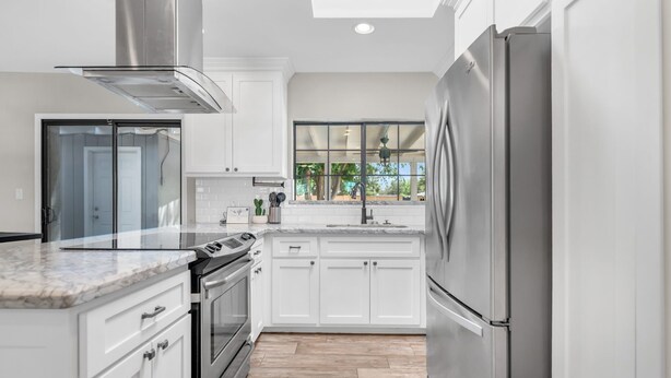A modern kitchen with white cabinetry, a stainless steel refrigerator, and a large window providing a view of the outdoors.
