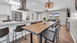 A modern kitchen with a large island, stainless steel appliances, and a dining area with a wooden table and bar stools.