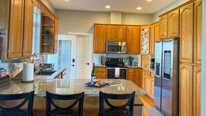 A kitchen with wooden cabinets, a granite countertop, a stainless steel refrigerator, and a microwave. - Lakefront Getaway with Game Room and Theater Seating (Moses Lake)