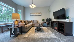A living room with a sofa, coffee table, lamp, TV, fireplace, and large windows. - Lakefront Getaway with Game Room and Theater Seating (Moses Lake)