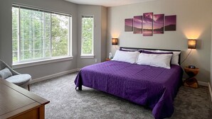 A bedroom with a large bed, two bedside tables, a chair, and a window. - Lakefront Getaway with Game Room and Theater Seating (Moses Lake)
