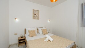 Un dormitorio ordenado con cama, mesitas de noche, una lámpara colgante y una obra de arte en la pared.
