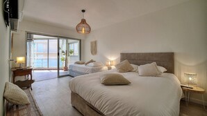 Een ruime slaapkamer met een groot bed, twee nachtkastjes met lampen, een bankje en uitzicht op het omliggende landschap via een schuifdeur.