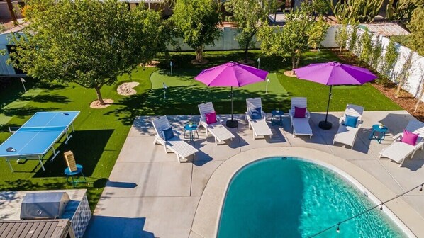 Un patio trasero con piscina, sillas de descanso y mesa de ping pong.