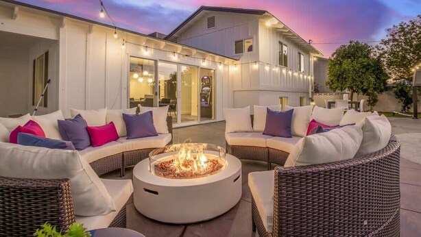 Un espacio de estar al aire libre con mobiliario de mimbre y una chimenea central.