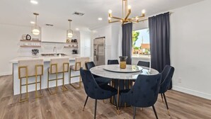 Una cocina moderna con armarios blancos, una isla central con taburetes y una mesa redonda con sillas.