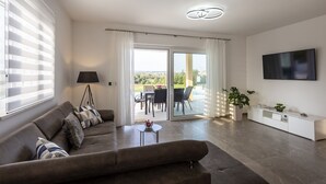 Una sala moderna con un sofá, una mesita de centro, un televisor y un balcón con mobiliario exterior.