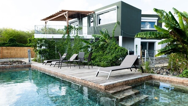 A modern house with a swimming pool, lounge chairs, and a wooden deck.