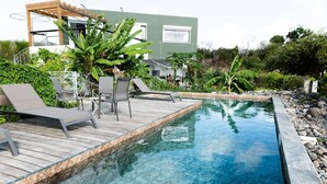 A modern pool area with lounge chairs, a wooden deck, and a clear pool.