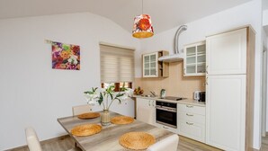 Een moderne keuken met witte kasten, een houten eettafel met geweven placematen en een bloemenlichtarmatuur.