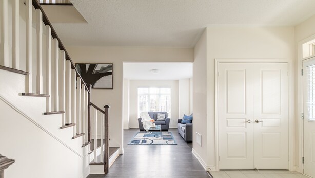 Un couloir avec un escalier, un salon avec un canapé et une table basse, et une porte blanche.