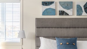 Une chambre à coucher comprenant un lit, une table de chevet, une lampe et trois œuvres d’art abstraites accrochées au mur.