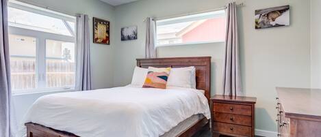 A bedroom with a wooden bed, a nightstand, a dresser, and a window with curtains.