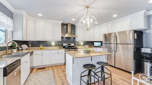 A modern kitchen with white cabinets, a stainless steel refrigerator, a gas stove, and a chandelier.