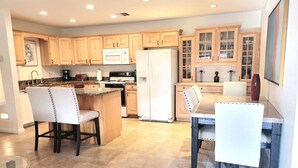 Una cocina con armarios de madera, un refrigerador blanco, una mesa de comedor con sillas y piso de baldosas.