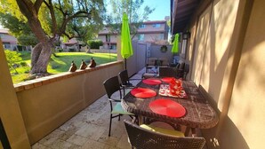 Un patio al aire libre con una mesa, sillas, un paraguas verde y vistas a un barrio residencial.