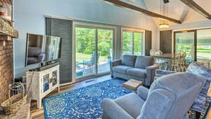 A spacious living room with a television, grey sofas, a patterned rug, and large sliding glass doors leading to a patio. - Breezy Silver Lake Getaway: Fishing Dock, Grill! (Mears)