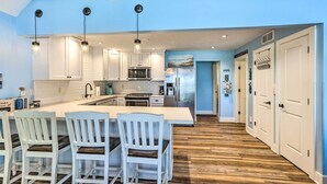 A kitchen with white cabinets, a central island with bar stools, stainless steel appliances, and a wooden floor. - Breezy Silver Lake Getaway: Fishing Dock, Grill! (Mears)