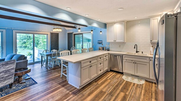 A modern kitchen with a large island, white cabinetry, and a dining area with a table and chairs. - Breezy Silver Lake Getaway: Fishing Dock, Grill! (Mears)