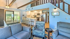 A spacious living area with a large sofa, a patterned armchair, and a dining table with chairs. A kitchen with modern appliances is visible in the background. - Breezy Silver Lake Getaway: Fishing Dock, Grill! (Mears)