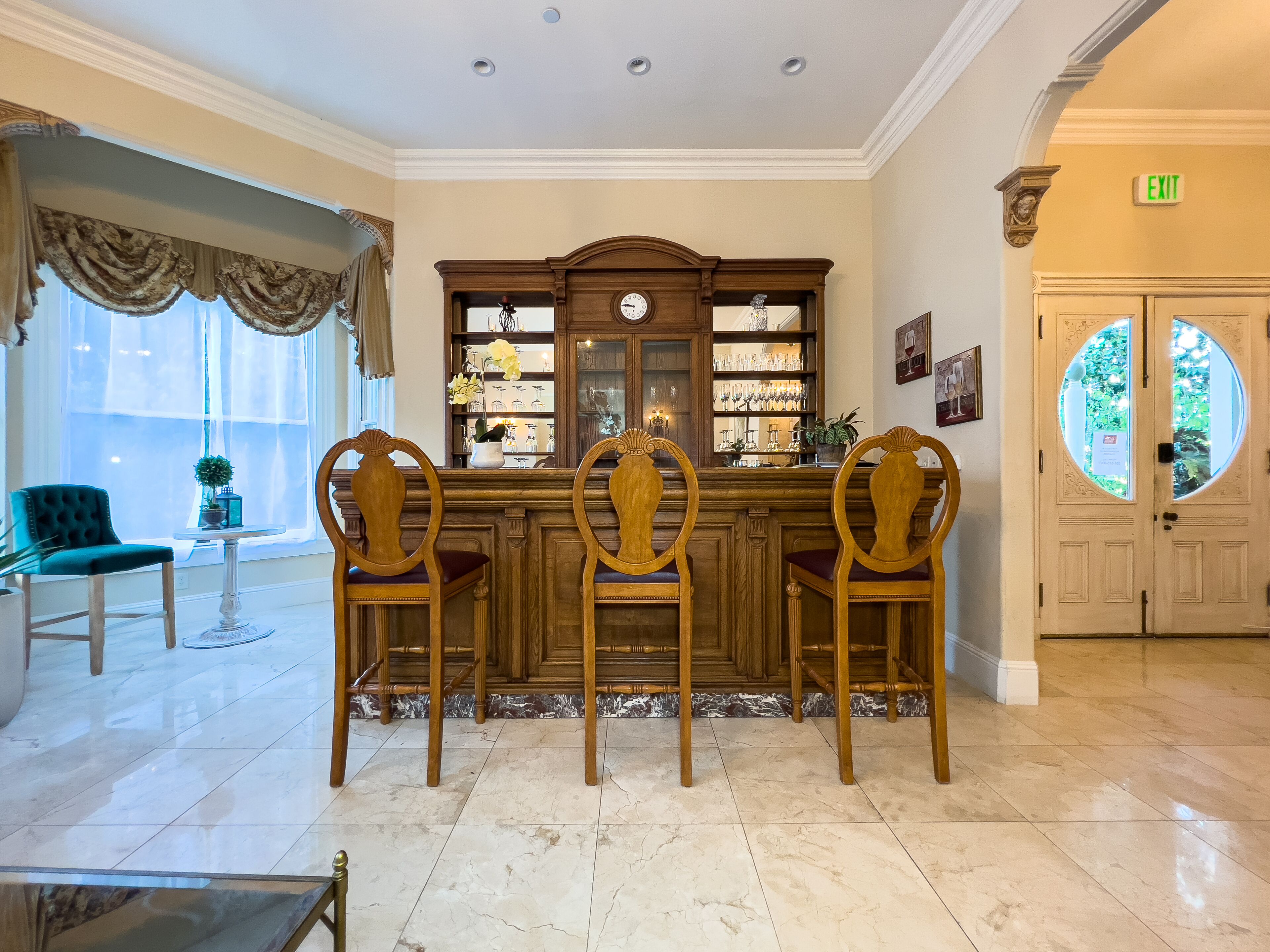 A bar area with a wooden counter, three wooden chairs, and a marble floor.