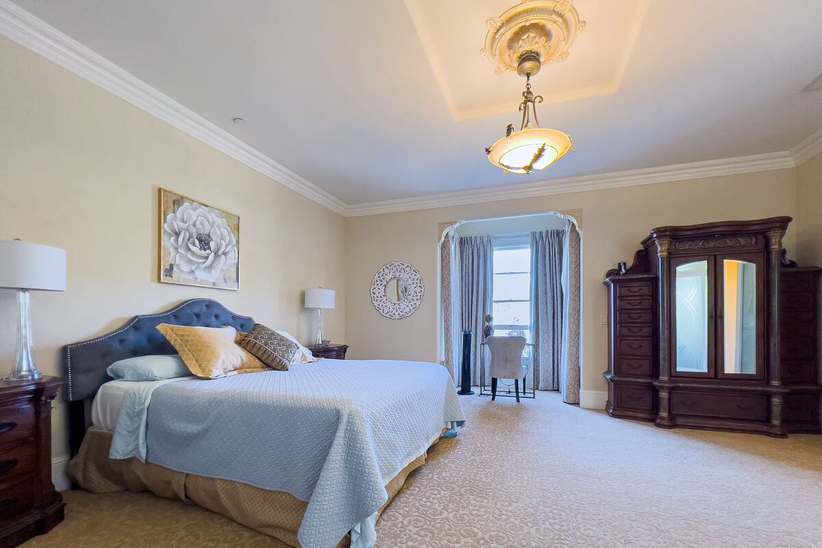 A bedroom with a large bed, a desk, a chair, a wardrobe, and a chandelier.