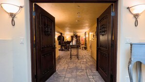 A hotel entrance with two large wooden doors, a sign above reading "CHATEAU CORALINI CELLARS", and a stone-tiled floor leading to a dining area with a table and chairs. - Chateau Coralini (Salinas)