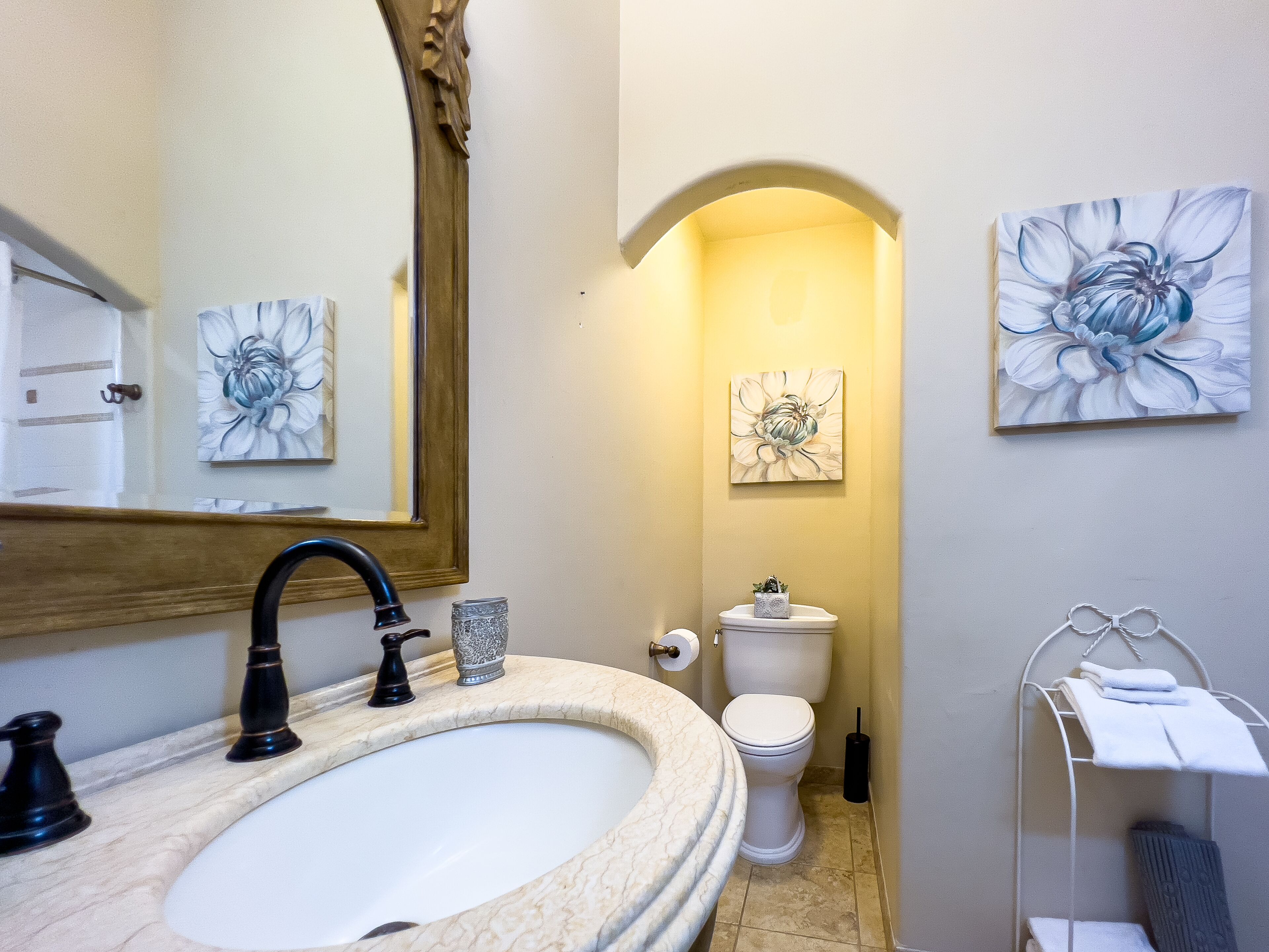 A bathroom with a marble sink, a large mirror, a toilet, and two floral paintings on the walls.