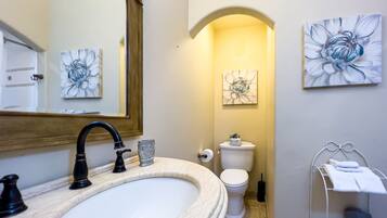 A bathroom with a marble sink, a large mirror, a toilet, and two floral paintings on the walls.