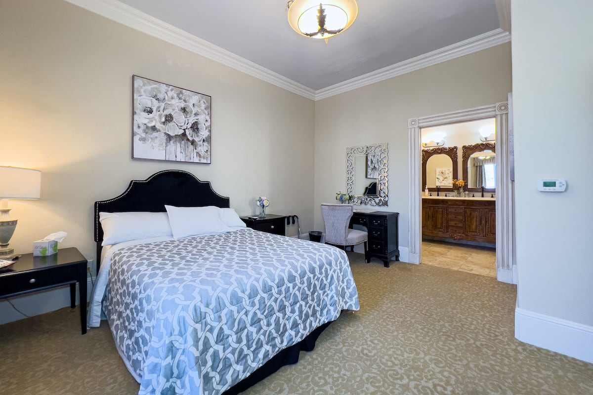 A hotel room with a bed, bedside table, lamp, dresser, mirror, and a door leading to a bathroom.