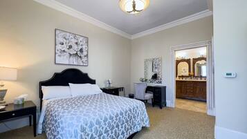 A hotel room with a bed, bedside table, lamp, dresser, mirror, and a door leading to a bathroom.