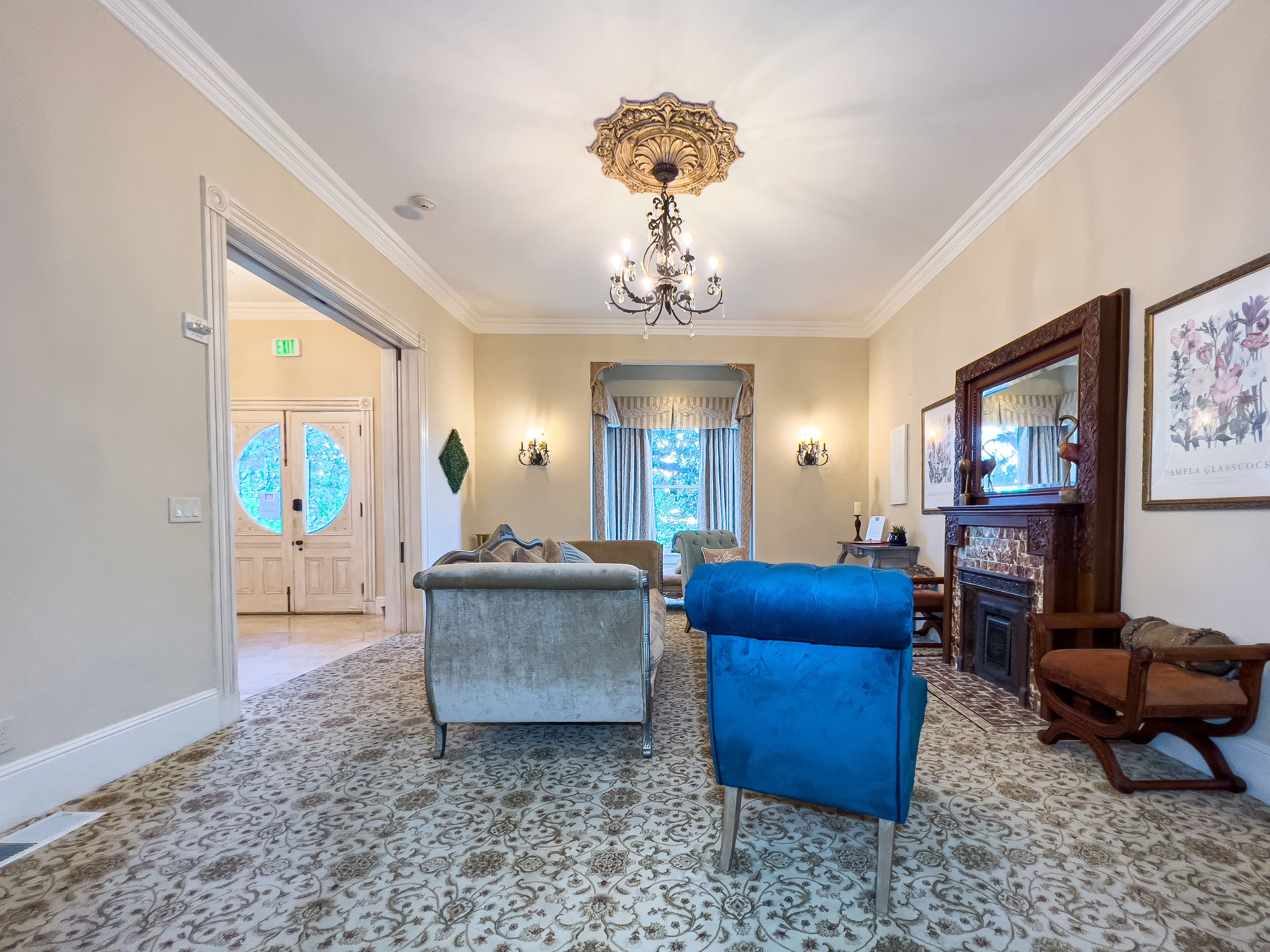A spacious living room with a chandelier, a blue armchair, and a fireplace.
